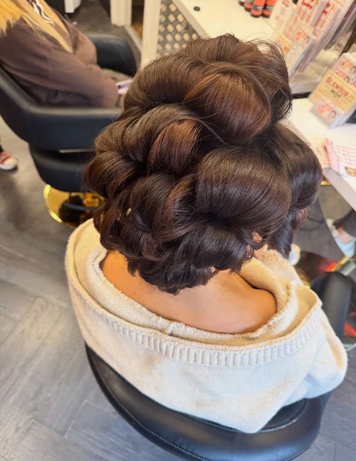 Back view of dark hair styled into a pin-curl set updo with smooth, sculpted rolls.