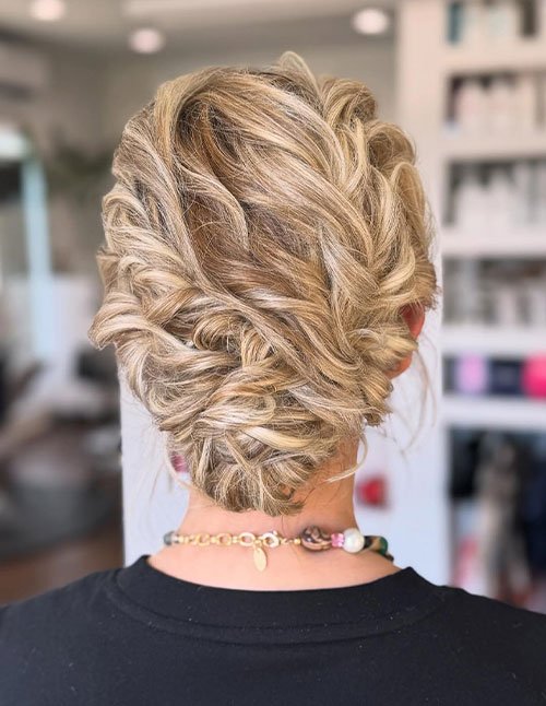 Back view of blonde hair styled into a low, twisted pinned updo with soft volume.