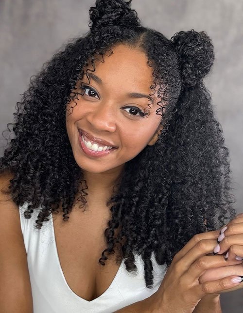 Playful double curly space buns with loose natural curls and face-framing tendrils
