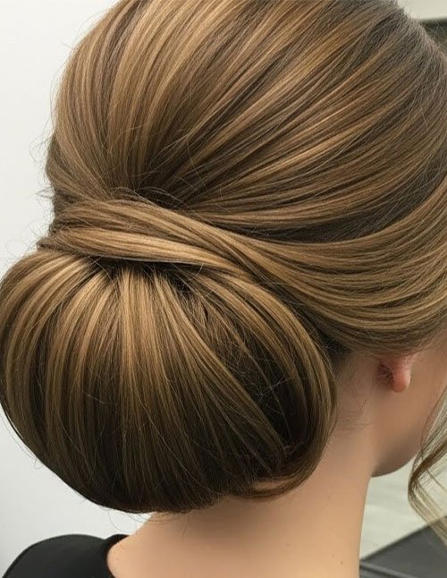 Side view of a polished low bun with smooth, wrapped sections and subtle highlights, styled neatly at the nape for a sleek formal look.