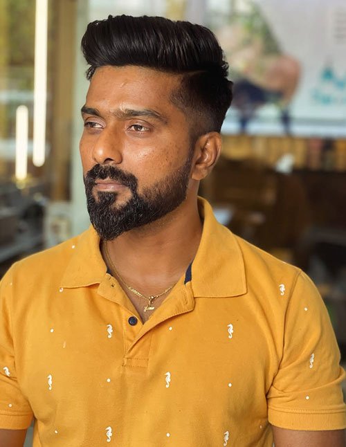 Man with a modern pompadour hairstyle, high volume front, faded sides, and a groomed beard.