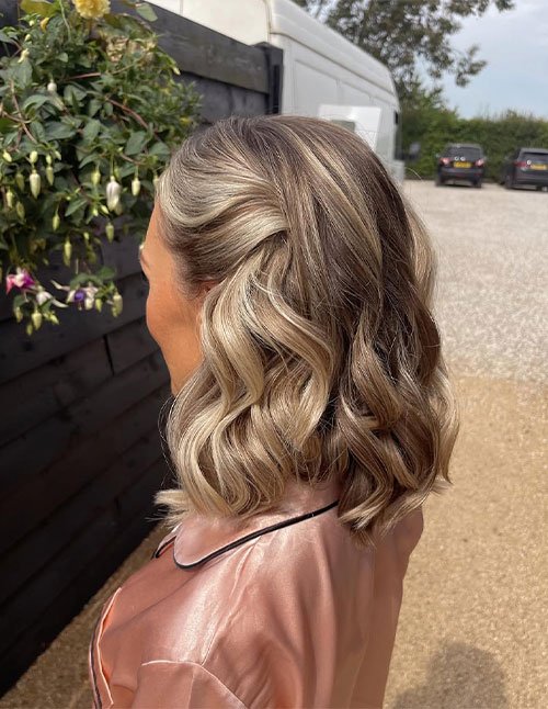 Side view of a woman wearing a prom hairstyle for short hair, styled with soft loose waves and a subtle side twist pinned back.