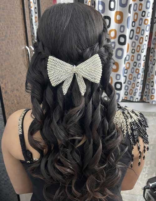 Prom-ready braided half-up hairstyle with soft curls, finished with a pearl bow accessory and loose flowing lengths.