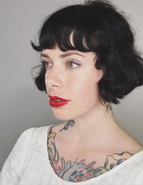 Side-profile of a razor-cut French bob with short fringe on dark hair.