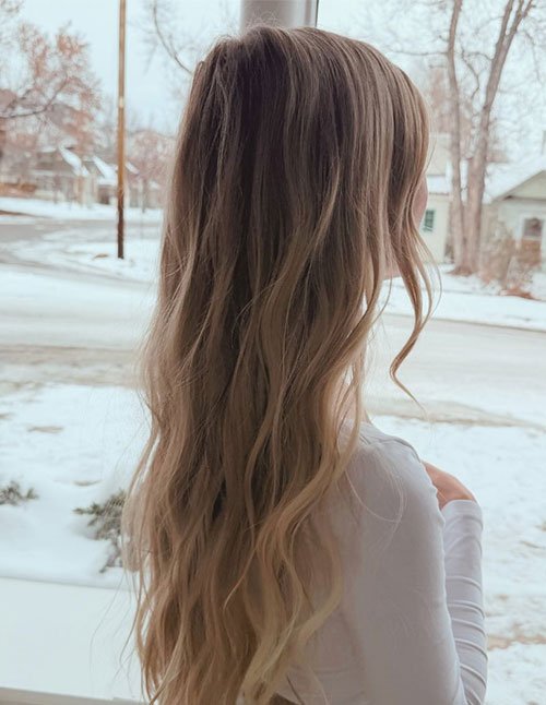 One girl with long, soft wavy hair worn down, standing by a window and looking outside at a snowy winter street.