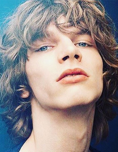 Close-up of a man with a shag haircut featuring messy layers, textured fringe, and a slightly longer mullet-like back.