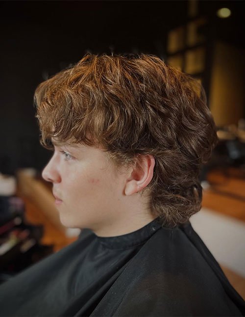 Side-profile of a teen with a shaggy wolf shag haircut, featuring choppy layers, a soft face-framing fringe, and longer textured length at the back.