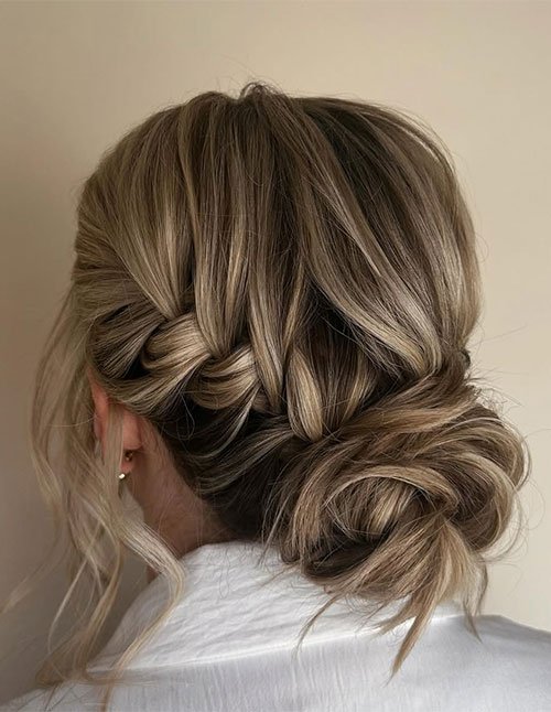 Back view of a short hair updo featuring a low twisted bun with softly braided sections and loose face-framing strands.