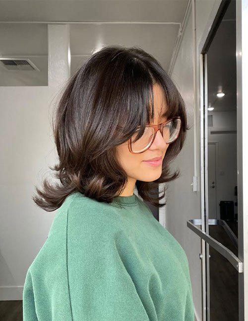 Woman with short layered haircut and soft curtain bangs, wearing glasses.
