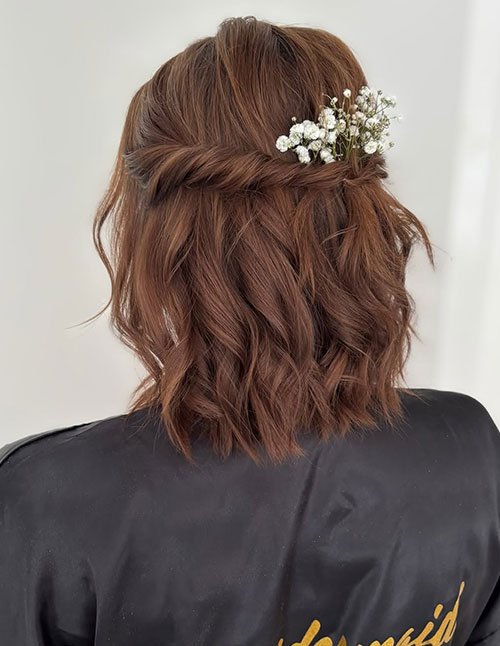 Short wedding hair styled half-up half-down with soft curls and a floral pin.