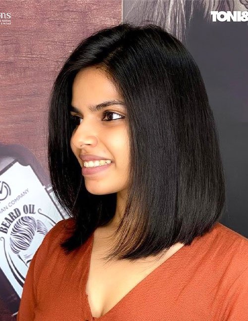 Woman with a sleek, straight bob haircut and a deep side part, with smooth, shiny hair falling to just above the shoulders.