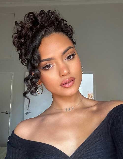 Close-up of a woman with a side-swept curly bun and a loose curl framing her face.