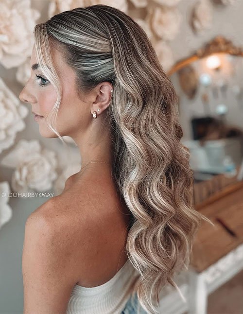 Side-swept glam waves on long blonde balayage hair with a soft face-framing strand.