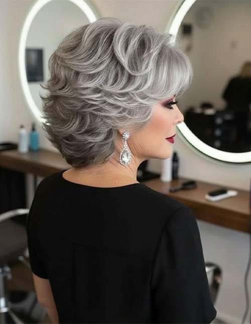 Silver-gray feathered pixie-bob with lifted crown volume, soft stacked layers, and a swept side fringe in a salon setting