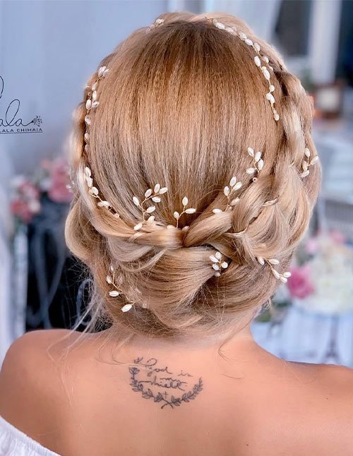 Back view of a woman with blonde hair styled in a simple braided crown wrapped around the head, finished with delicate pearl hair vines and a low tucked bun.