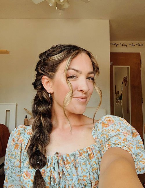 Woman wearing a simple side braid draped over one shoulder, with softly parted hair and loose face-framing strands for a relaxed, natural look.
