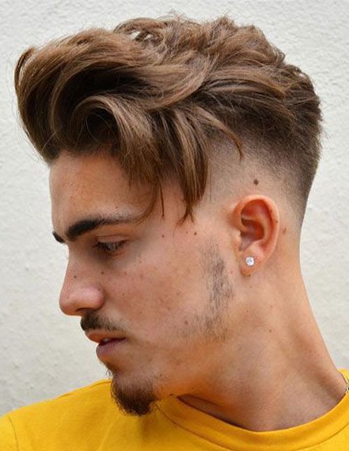 Side profile of a man with a skin fade featuring a smooth gradient, paired with a longer, wavy textured top swept forward and to the side.
