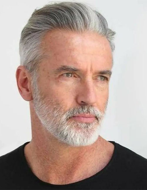 Older man with silver hair styled in a sleek slicked-back look, featuring a neat tapered cut on the sides and a full gray beard.