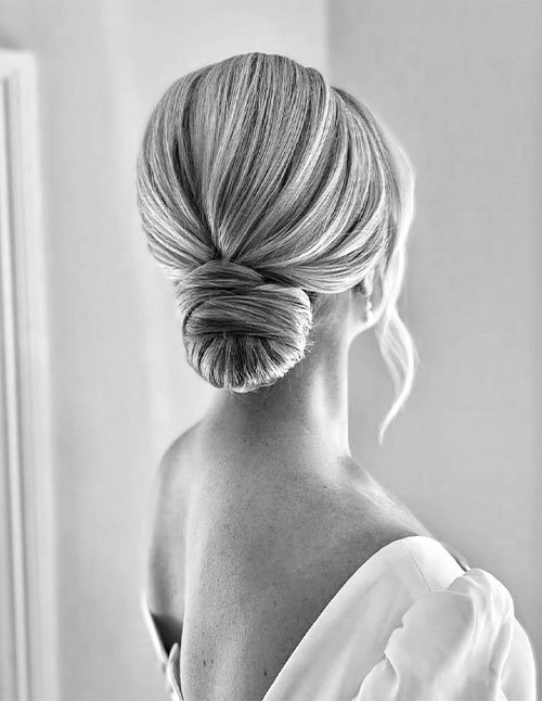 Woman with smooth, neatly styled hair pulled into a sleek low chignon at the nape, featuring a clean center part and polished finish.
