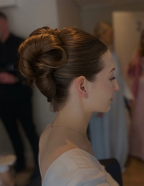 Sleek heavy-hair updo with a smooth crown and structured low bun, side profile.