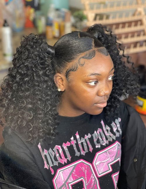 Side view of a girl with a sleek middle-part hairstyle styled into two high fluffy curly ponytails, with laid baby hairs and voluminous curls.