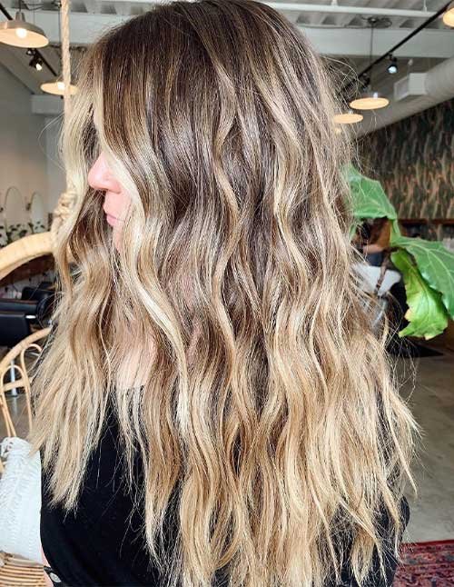 Side view of long hair styled in soft beach waves with blonde highlights.