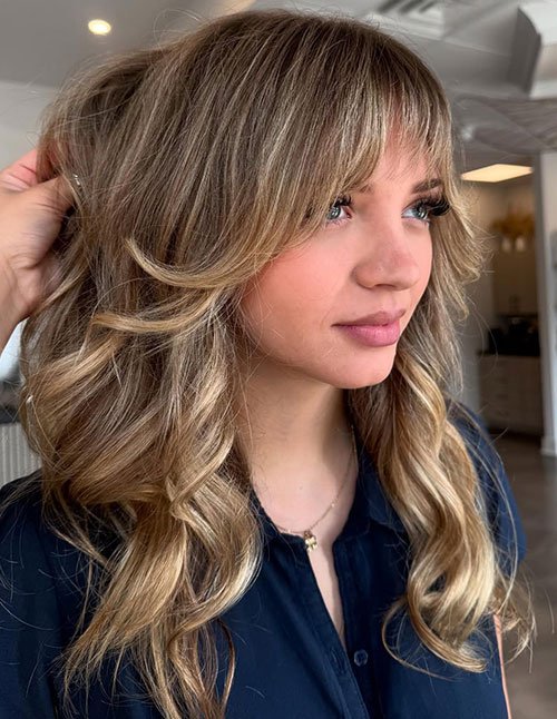 Blonde wavy hair with soft blended fringe and face-framing layers.