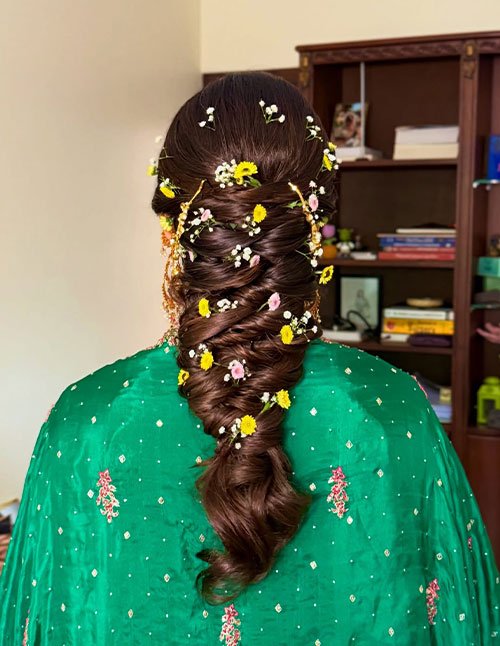 Soft braids styled into a thick, twisted braid down the back, decorated with small fresh flowers for a delicate finish.