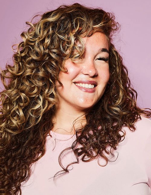 Smiling woman with long, soft defined curls and blonde highlights.