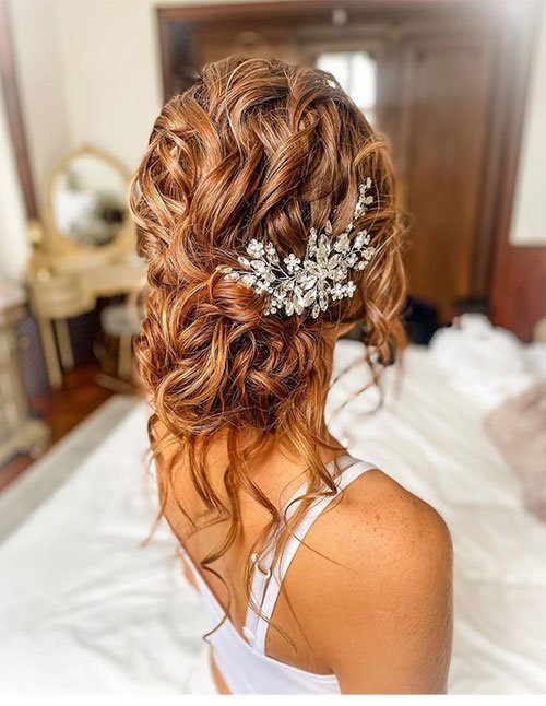 Soft curly bridal updo with floral crystal hair accessory and loose tendrils
