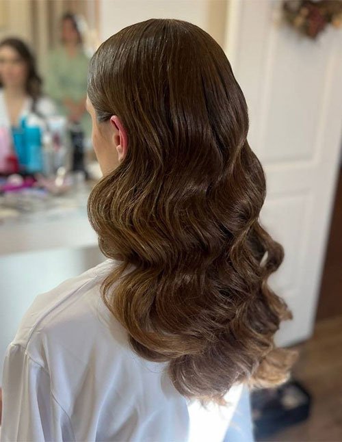 One girl with medium-to-long brown hair styled in smooth, soft waves, photographed from the back in an indoor dressing room setting.