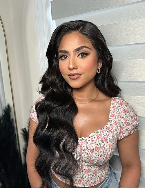One girl with long, glossy black hair styled in soft, side-swept Hollywood waves, wearing a floral top indoors.