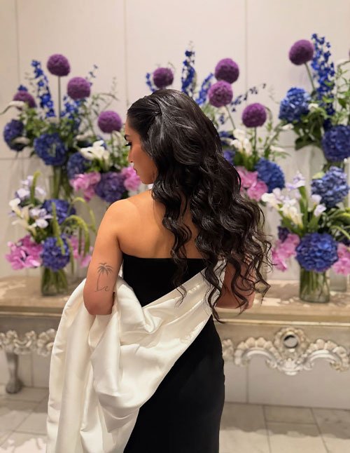 Girl with long, soft romantic curls styled in loose waves, shown from the back in an elegant black dress with a gentle side-swept flow.