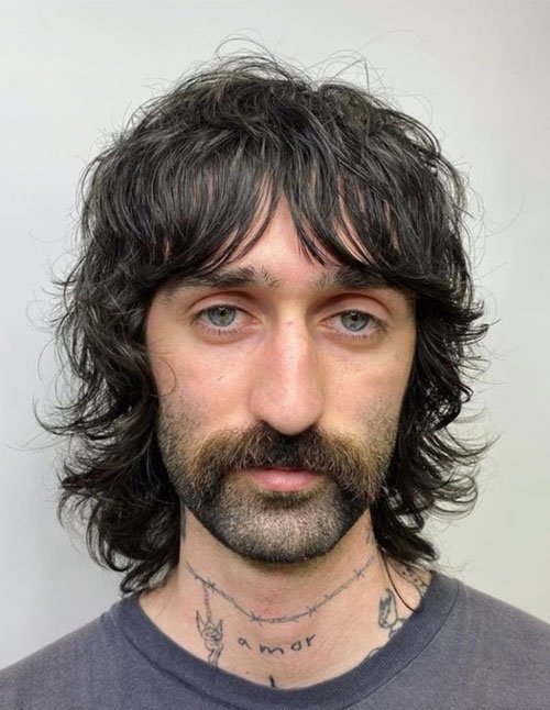 Front view of a man with a medium-length soft shag haircut, wispy bangs, and layered ends that flip out around the sides.