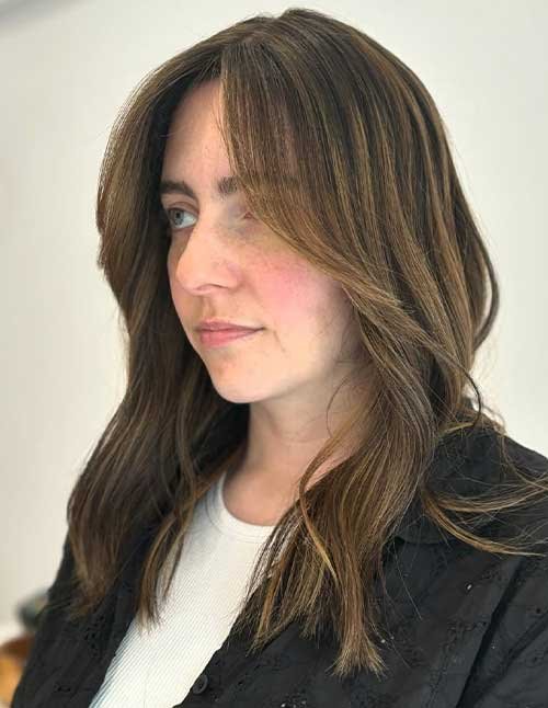 Side-profile of a woman with soft side-swept bangs and layered hair.