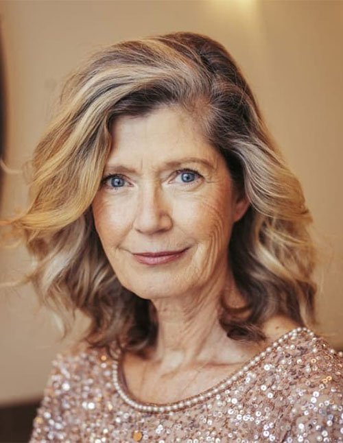 Soft side-swept wavy lob on mature woman with shoulder-length loose waves and blonde highlights
