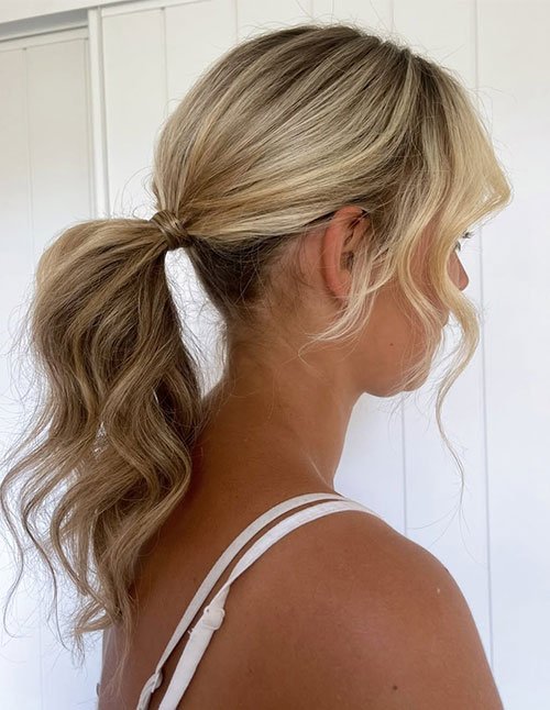 Woman with blonde hair styled in a soft textured ponytail, featuring loose natural waves, gentle volume at the crown, and face-framing strands for an effortless look.