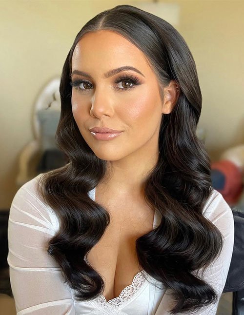 Woman with glossy dark hair styled in soft, loose waves, parted cleanly down the middle, creating a smooth and polished look with natural shine.