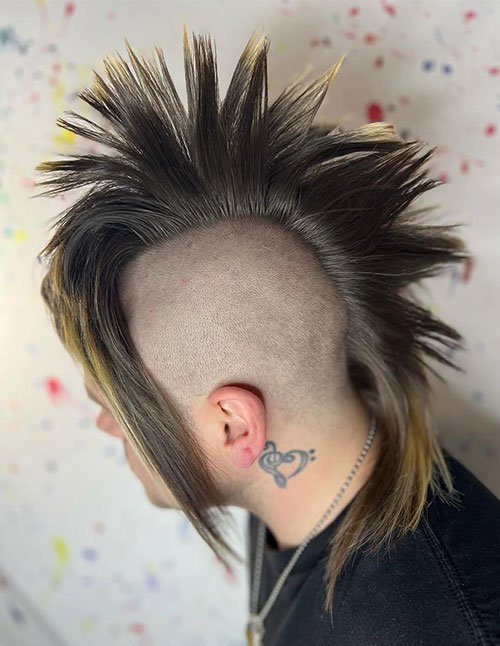 Side view of a person with a medium-length spiky mohawk, shaved sides, and long face-framing pieces, styled upward in sharp spikes.