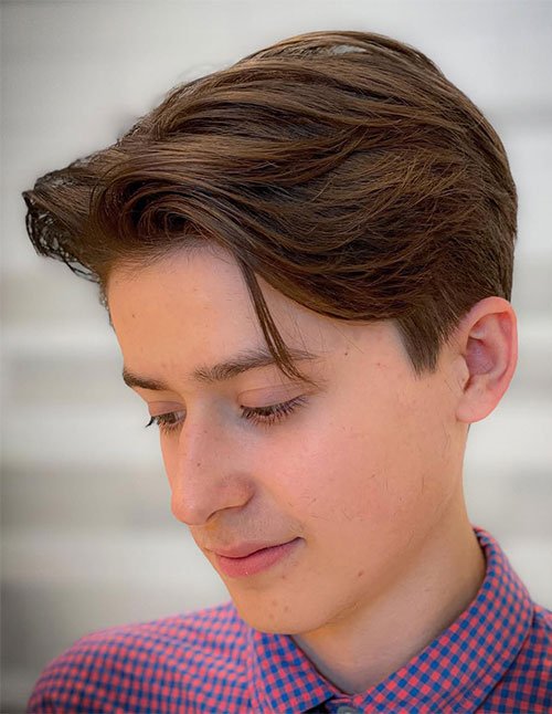 Young boy with a 90s-inspired side-swept haircut, featuring a textured scissor-cut top, clean tapered sides, and a soft fringe piece falling toward the forehead.