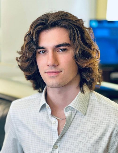 Man with a textured medium-length haircut featuring loose waves, layered volume, and a soft middle part framing the face.