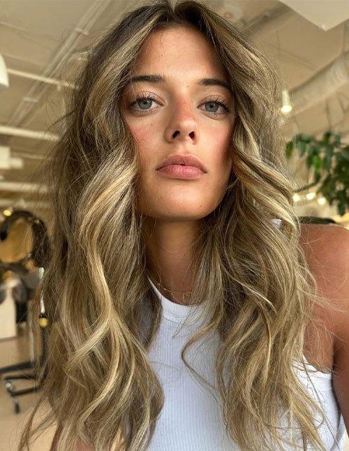 Woman with long textured wavy hair wearing a white top indoors