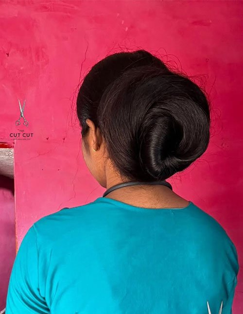 Back view of a woman with thick hair styled into a smooth, voluminous low bun at the nape.