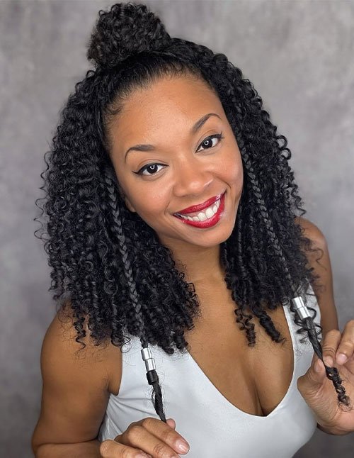 Front view of a woman with curly hair styled in a half-up top knot, with the rest of the curls left down and two twisted front pieces.