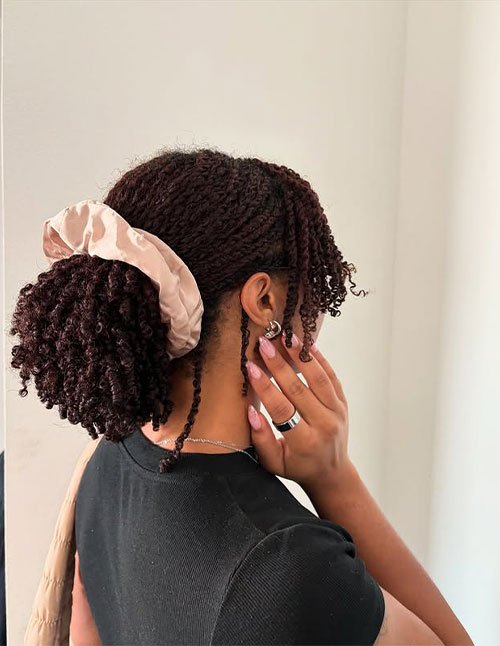 Side view of natural hair styled in a twist-out, gathered into a low puff with a satin scrunchie.