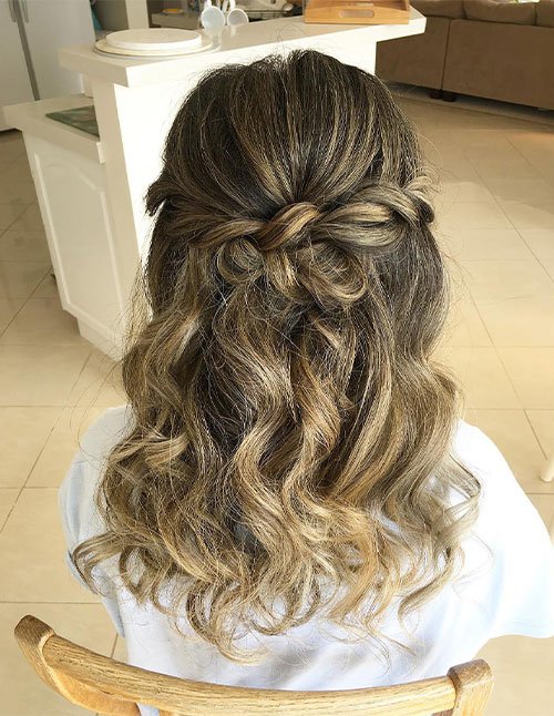 Back view of a girl with highlighted hair styled half-up with a twisted knot, and loose curls/waves cascading down.