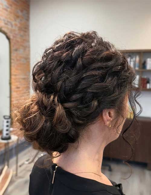Side view of a woman with a curly updo and a loose tendril, with a braided detail across the back of the head.