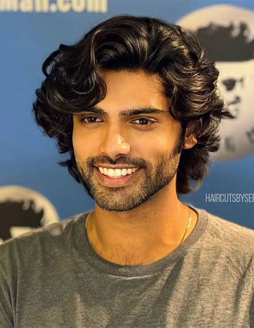 Man wearing a medium-length wavy hairstyle, featuring natural waves, layered volume, and a soft side-swept finish with a relaxed, polished look.