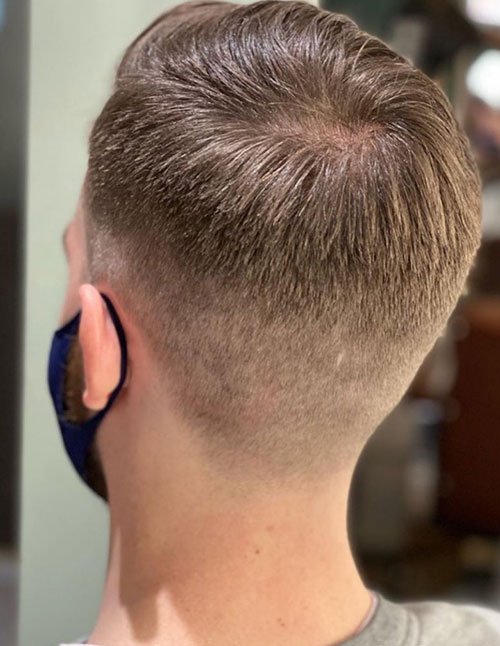 Back view of a man&rsquo;s haircut showing a clean winter low fade with short, neatly combed hair on top and tapered sides, wearing a face mask.