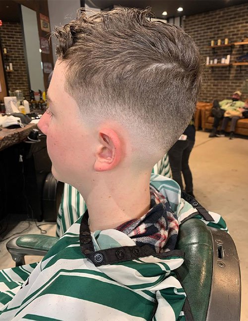 Side view of a man with a mid skin fade haircut, blending from shaved sides into a short, slightly textured top.